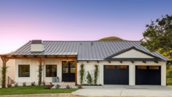 A white home with a metal roof and black garage doors