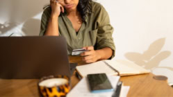 A stressed person sitting at a table with a credit card, laptop, and a cell phone